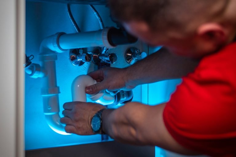 Plumber fitting pipes under a sink cabinet