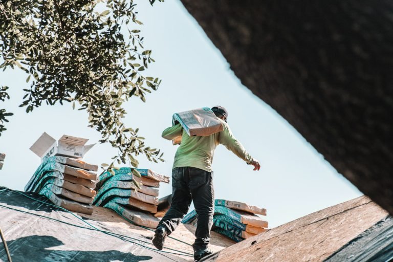Roofer carrying a bundle of shingles across a house roof